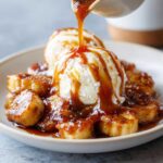 Close-up of caramelized bananas foster being topped with rich caramel sauce over scoops of vanilla ice cream.