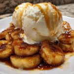 Close-up of warm, caramelized bananas foster topped with scoops of vanilla ice cream and caramel sauce.