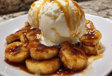 Close-up of warm, caramelized bananas foster topped with scoops of vanilla ice cream and caramel sauce.