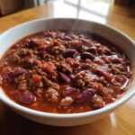 Close-up of a steaming white bowl filled with the best chili recipe, featuring ground beef and kidney beans in a rich red sauce.