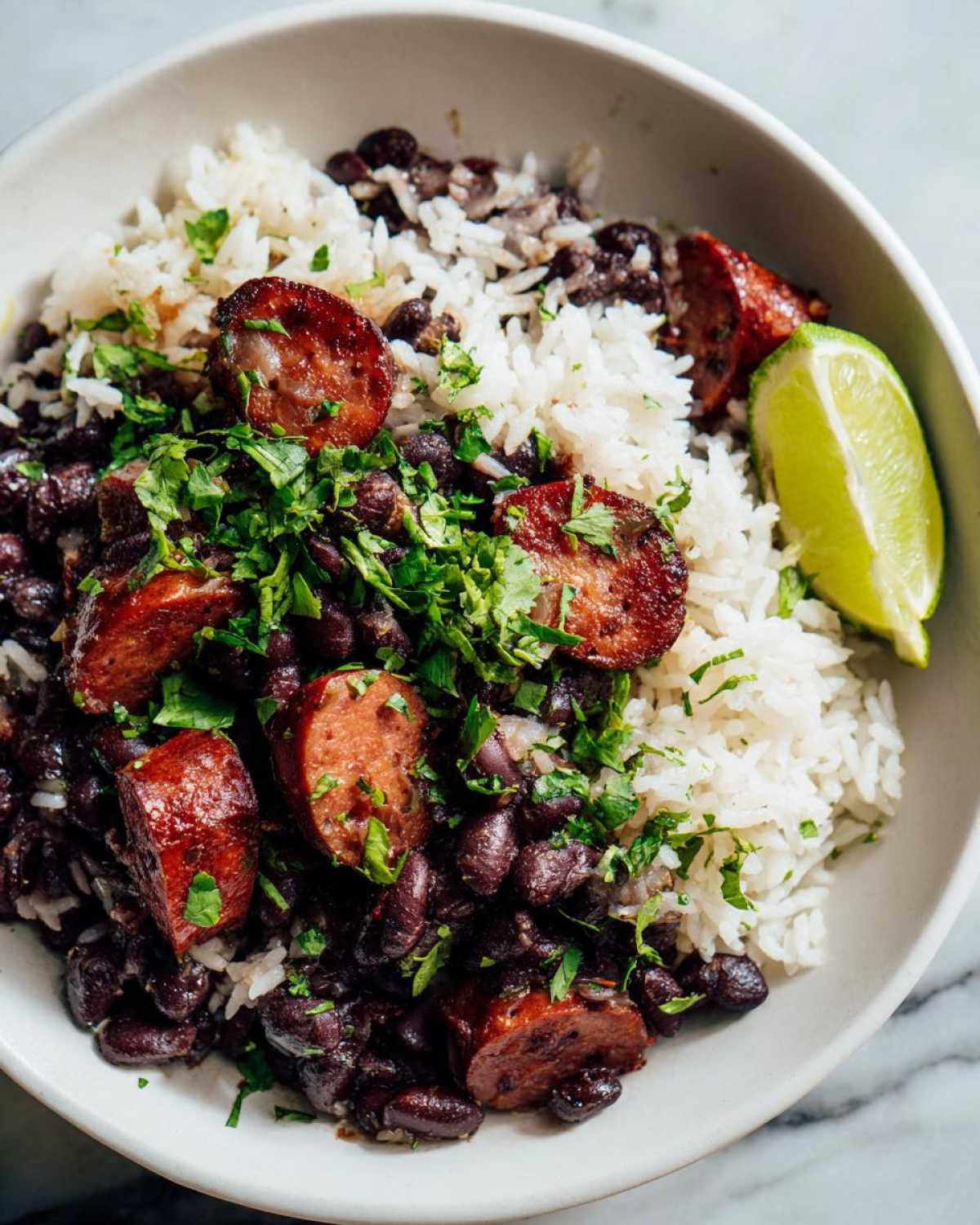 Close-up of a bowl of flavorful black beans and rice topped with sliced sausage and fresh cilantro.