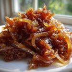 A close-up shot of a mound of deeply browned and glistening caramelized onions served on a white plate.