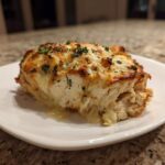 A thick, cheesy serving of baked caesar chicken topped with browned cheese and parsley.