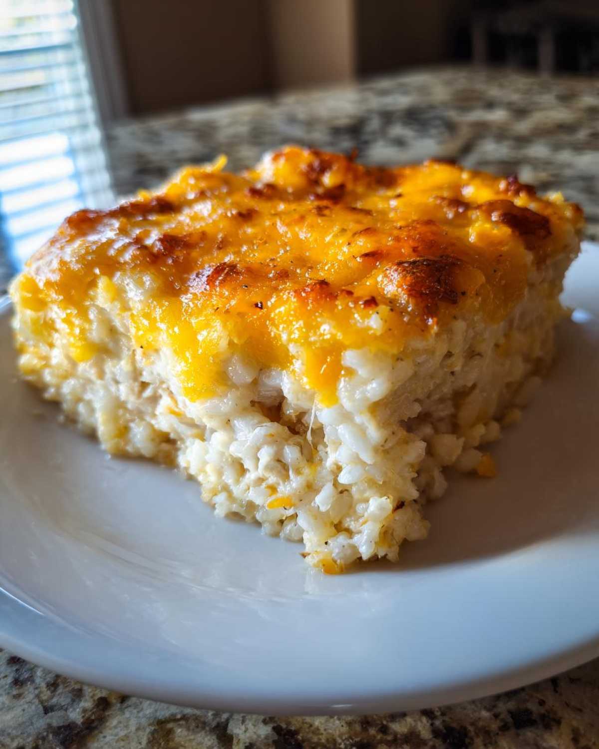 A square serving of cheesy chicken and rice casserole with a golden, melted cheese topping.