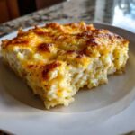 A square serving of creamy, baked cheesy chicken and rice with a golden-brown, bubbly cheese topping.