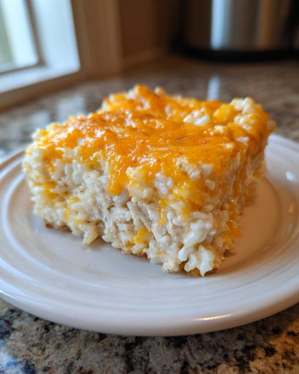 A square serving of baked cheesy chicken and rice casserole topped with melted cheddar cheese.