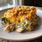 A close-up of a serving of creamy chicken broccoli rice casserole topped with melted cheddar cheese and crunchy breadcrumbs.
