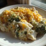 A close-up serving of creamy chicken broccoli rice casserole topped with melted cheddar cheese and breadcrumbs.