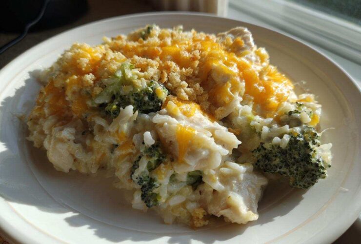 A close-up serving of creamy chicken broccoli rice casserole topped with melted cheddar cheese and breadcrumbs.