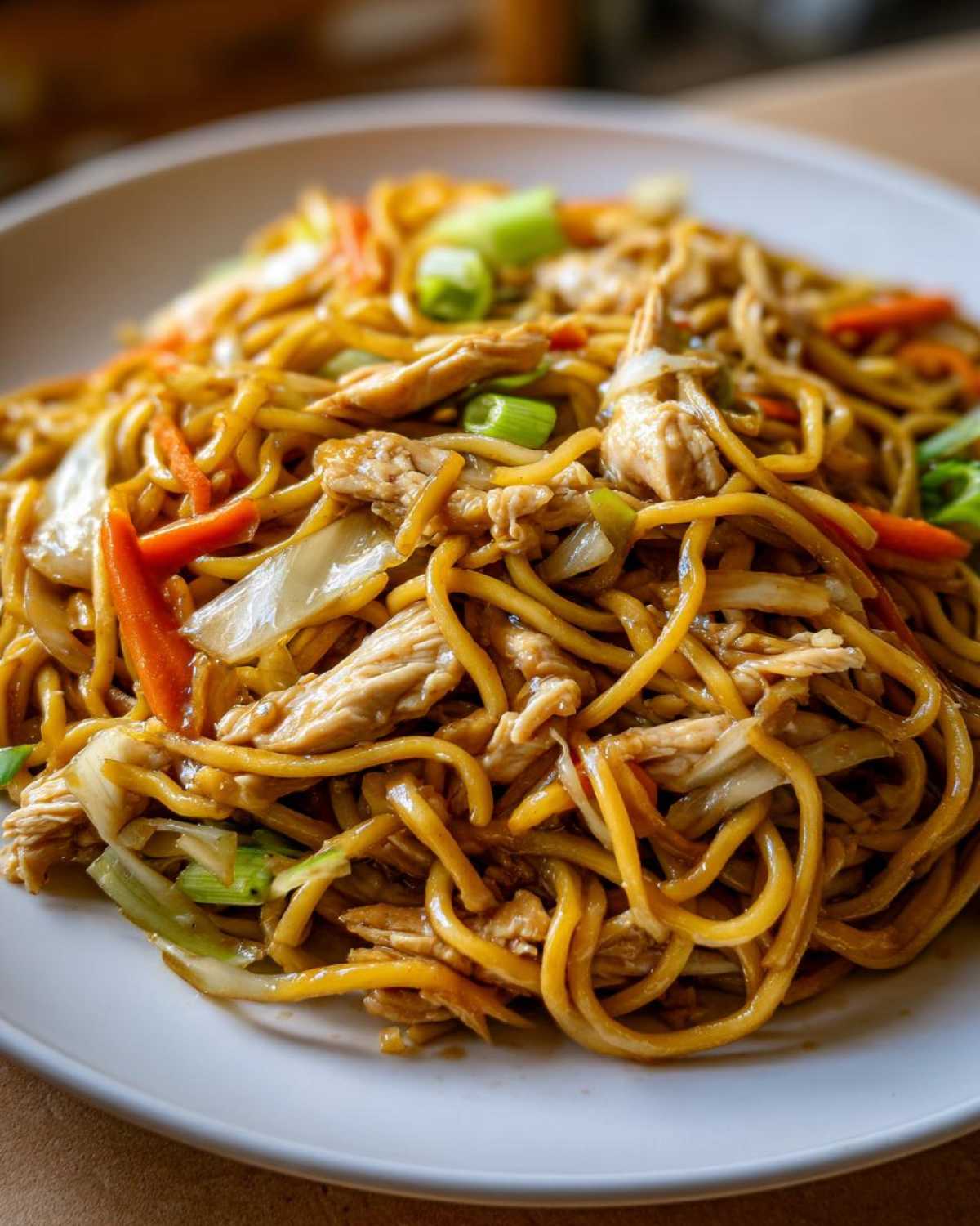 Close-up of a plate piled high with delicious chicken chow mein recipe noodles, shredded chicken, and vegetables.