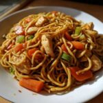 Close-up of a serving of flavorful chicken chow mein recipe with noodles, sliced carrots, and celery.