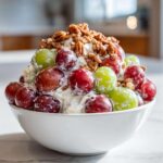 A close-up of a creamy chicken salad chick grape salad, topped generously with red and green grapes and pecans.