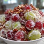 A close-up of creamy chicken salad chick grape salad, featuring red and green grapes coated in dressing and topped with pecans.