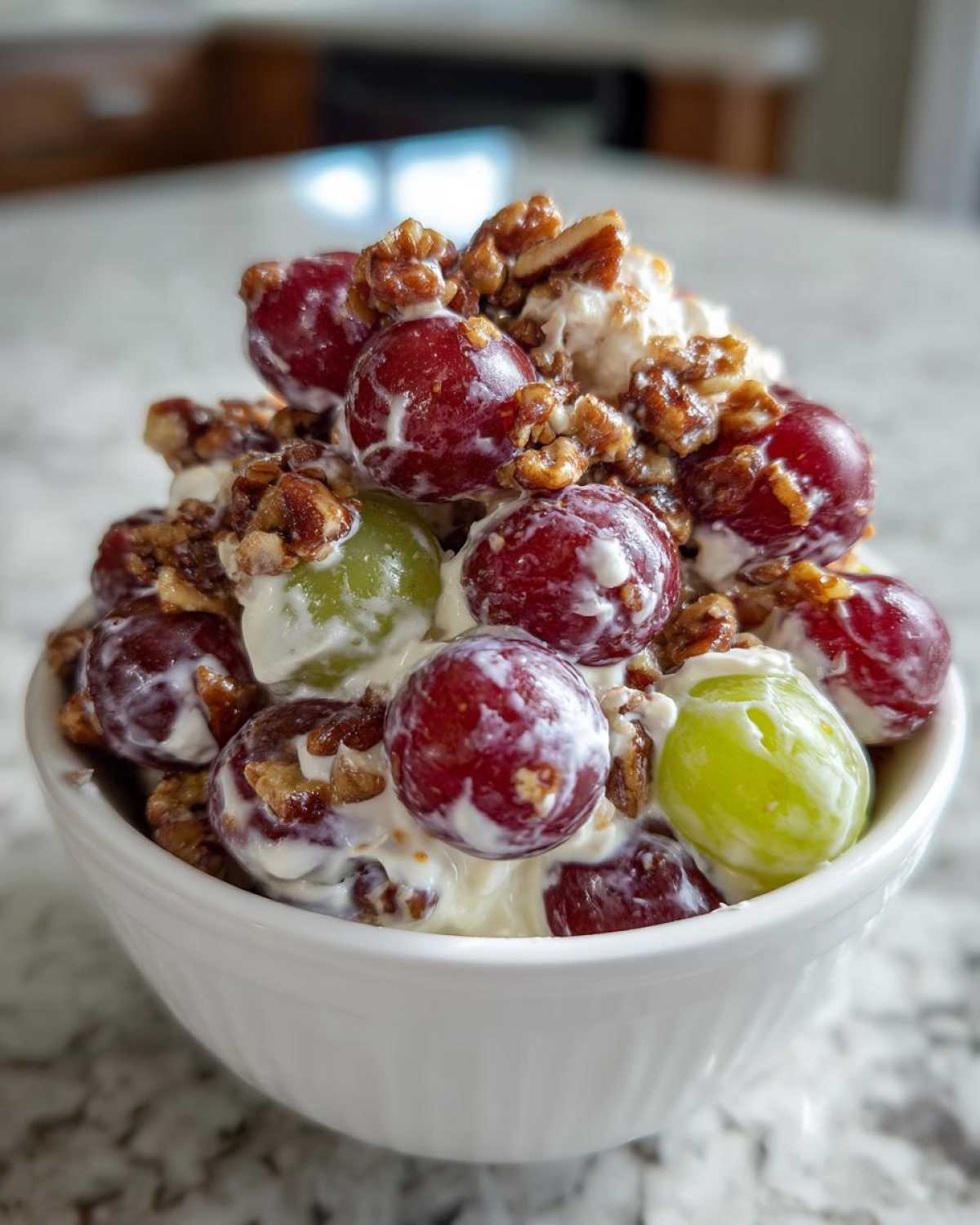 A small white bowl filled with creamy chicken salad chick grape salad, topped with red and green grapes and candied pecans.