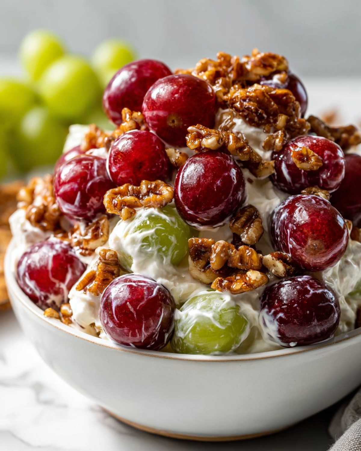 A close-up of creamy chicken salad chick grape salad topped with red and green grapes and candied pecans.