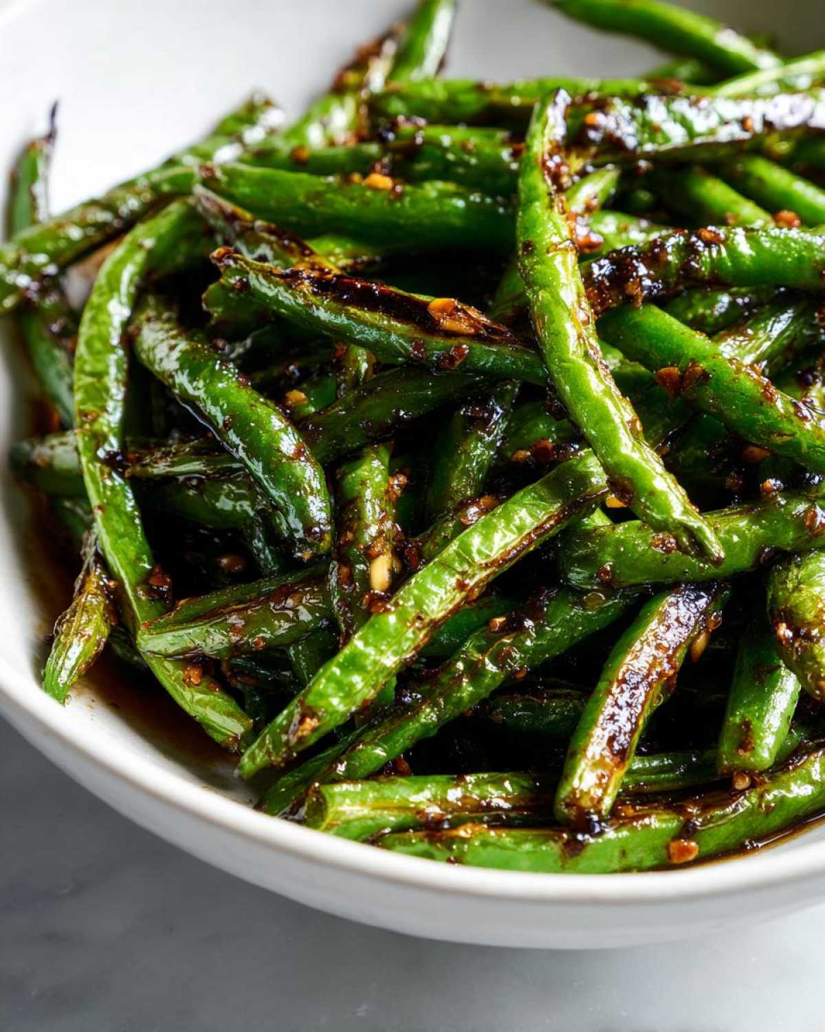 Close-up of vibrant green beans coated in a dark, glossy garlic sauce, ready to serve.