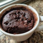 Close-up of a rich, dark chocolate mug cake topped with chocolate chips, served in a white mug.