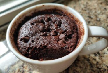 Close-up of a rich, dark chocolate mug cake topped with chocolate chips, served in a white mug.
