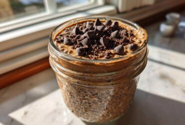 Close-up of chocolate overnight oats in a mason jar topped with chocolate chips, sitting by a sunny window.