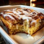 Close-up of a square serving of moist cinnamon roll casserole topped with thick white icing.