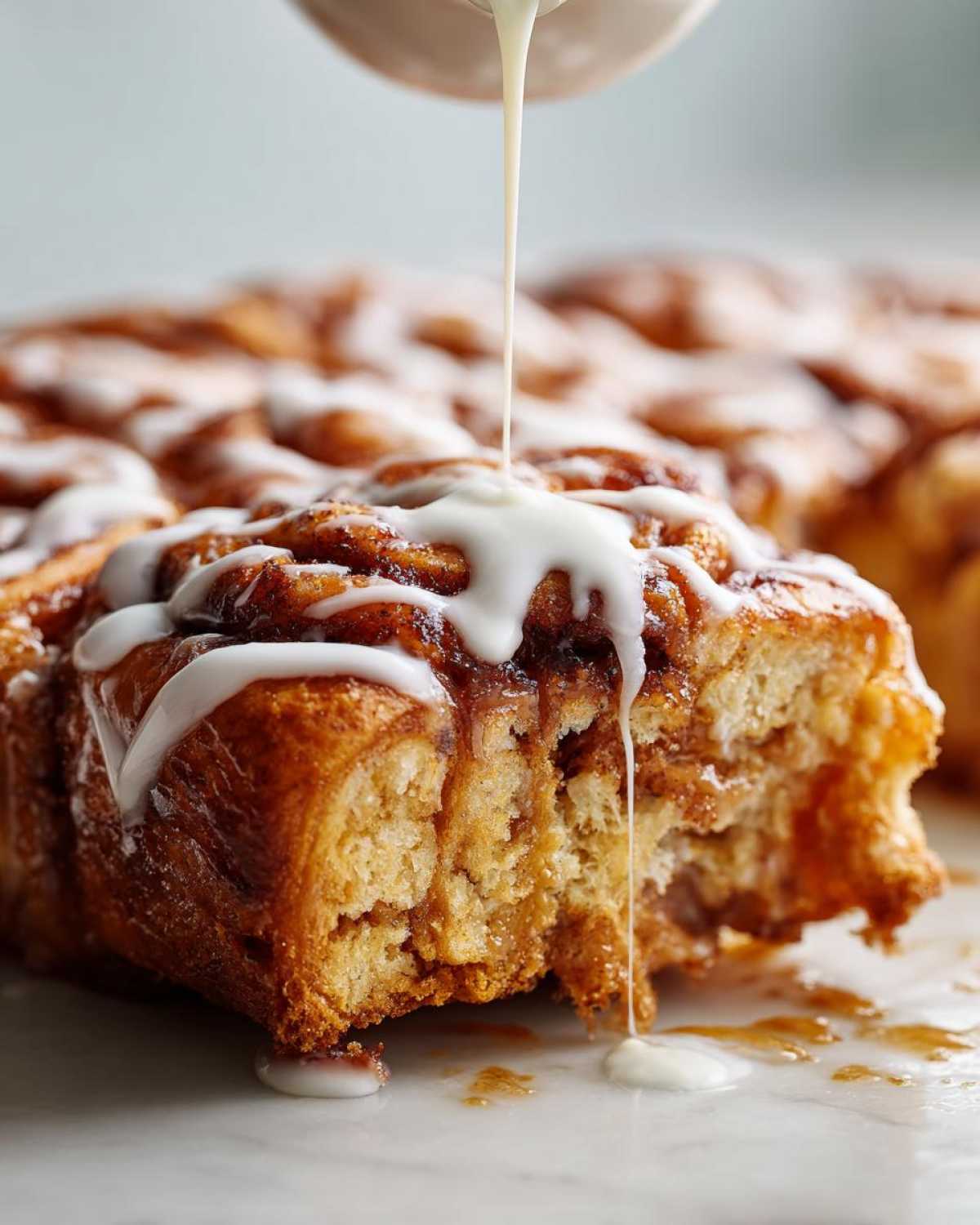Close-up of thick white icing being drizzled over a soft, baked Cinnamon roll casserole.