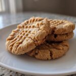A stack of four classic peanut butter cookies showing the traditional crisscross fork marks.