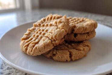 A stack of four classic peanut butter cookies showing the traditional crisscross fork marks.
