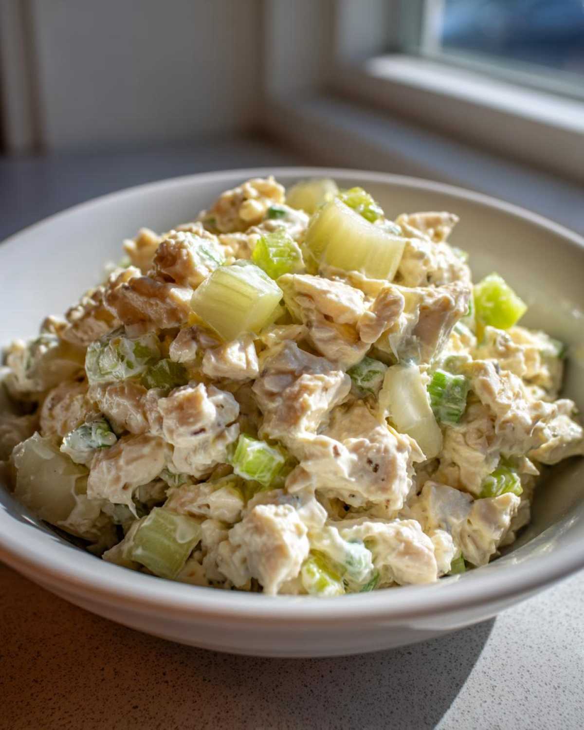 A close-up of a white bowl filled with creamy cottage cheese chicken salad mixed with visible chunks of celery.