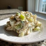 A scoop of creamy cottage cheese chicken salad mixed with visible chunks of celery on a white plate.