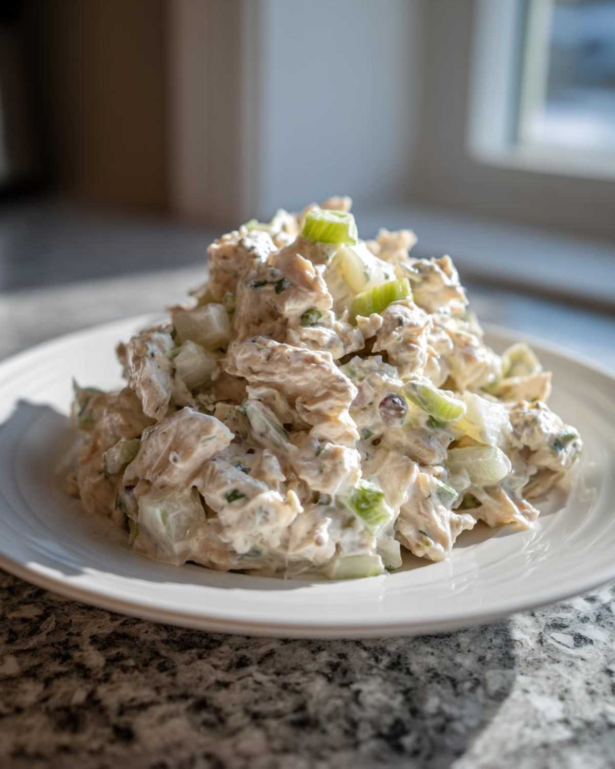 A scoop of creamy cottage cheese chicken salad mixed with chopped celery on a white plate.
