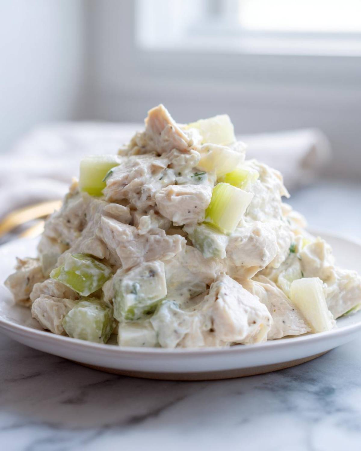 A mound of creamy cottage cheese chicken salad mixed with visible chunks of celery, served on a white plate.