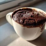 Close-up of a fudgy Cottage Cheese Microwave Brownie baked in a white mug, topped with chocolate chips.