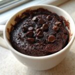 Close-up of a fudgy Cottage Cheese Microwave Brownie topped with chocolate chips in a white mug.