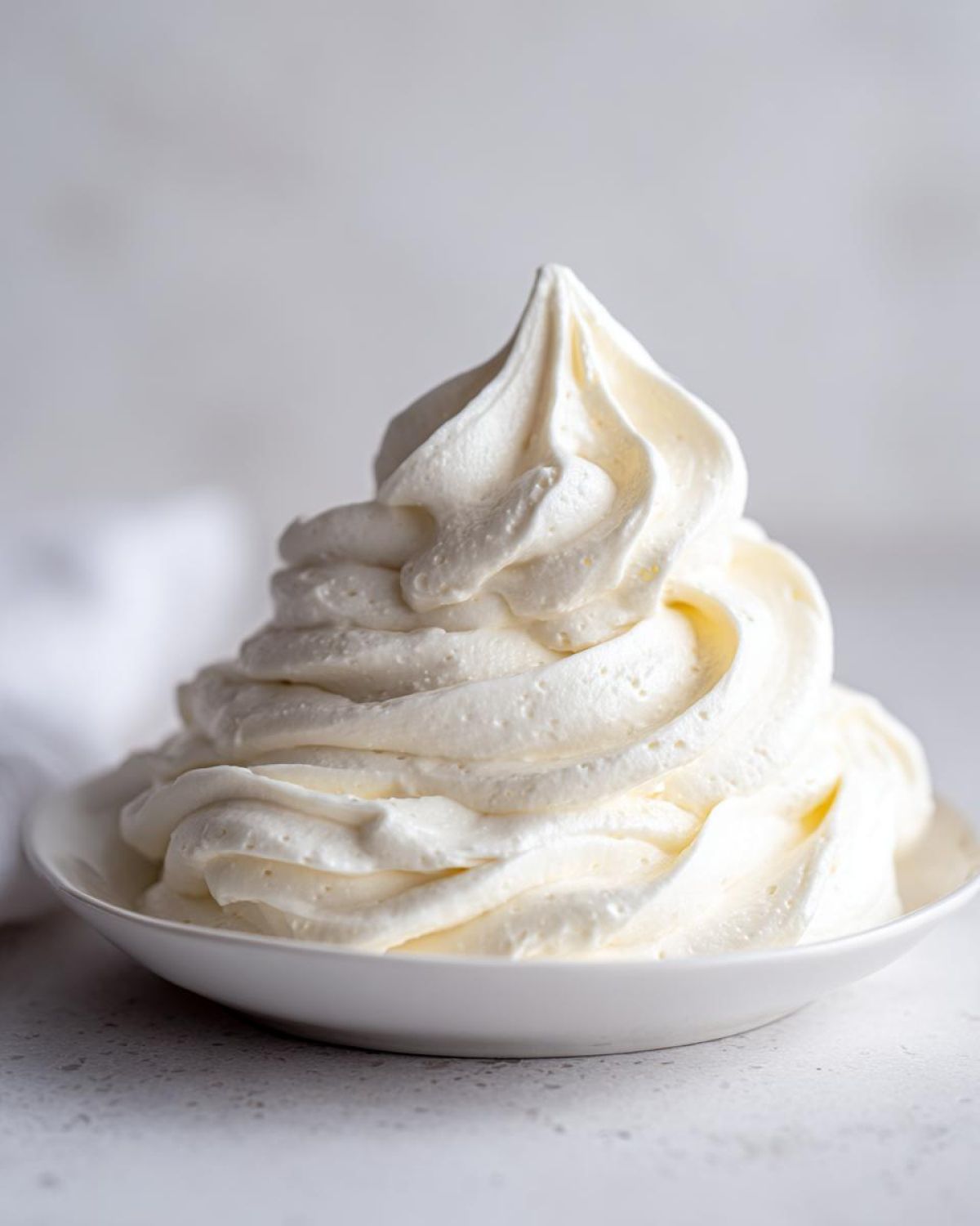 A tall, perfectly piped swirl of fluffy white cream cheese frosting sitting in a small white bowl.