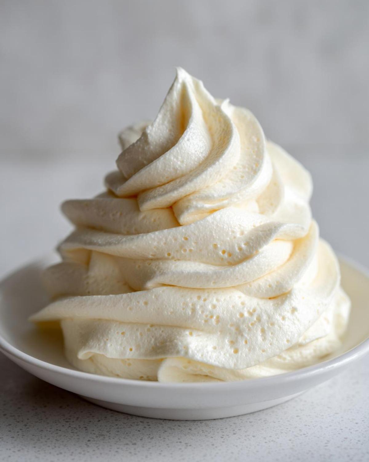 A beautiful, tall swirl of fluffy, pale yellow cream cheese frosting piped into a small white bowl.