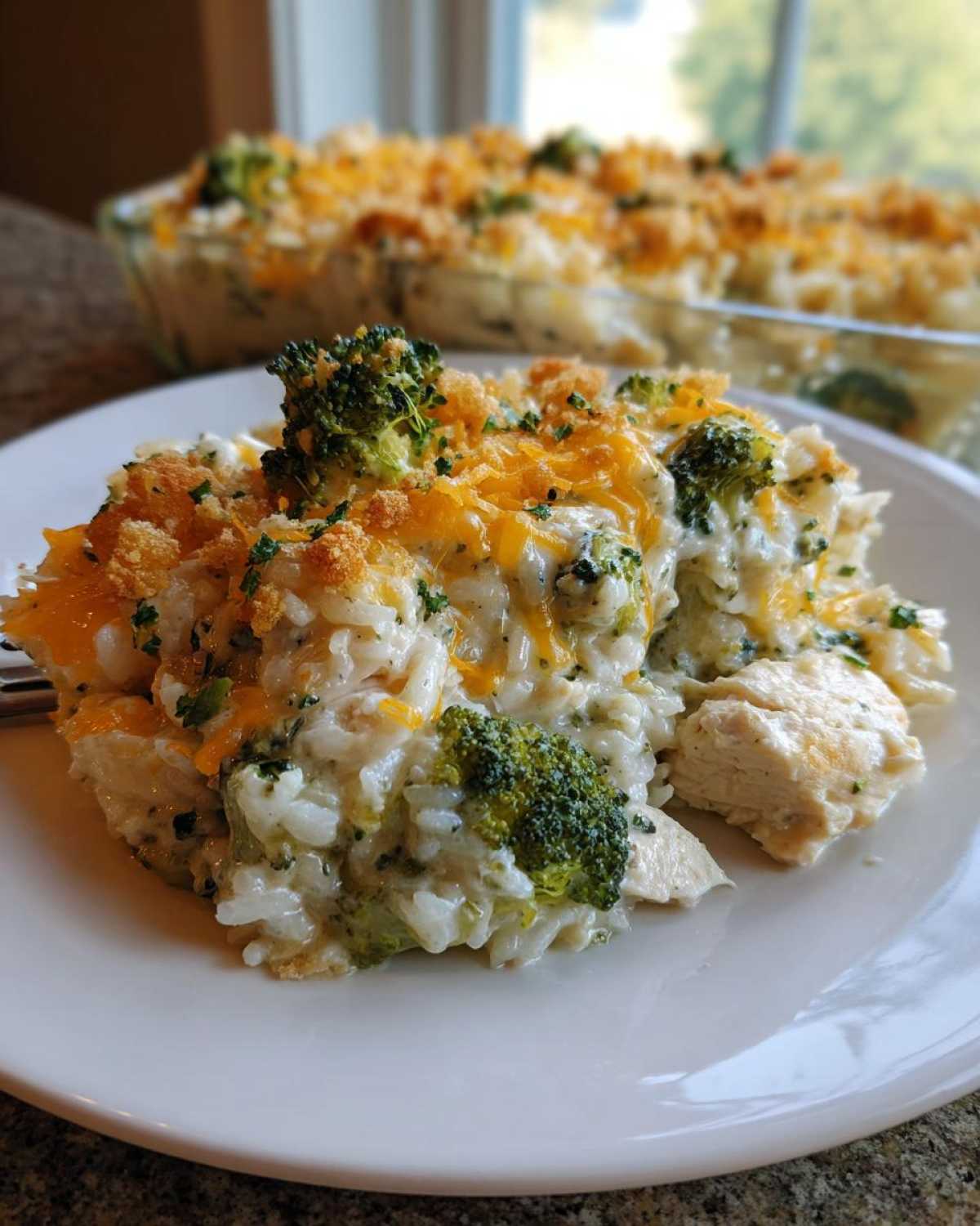 A close-up serving of creamy chicken broccoli rice casserole topped with melted cheddar and breadcrumbs.