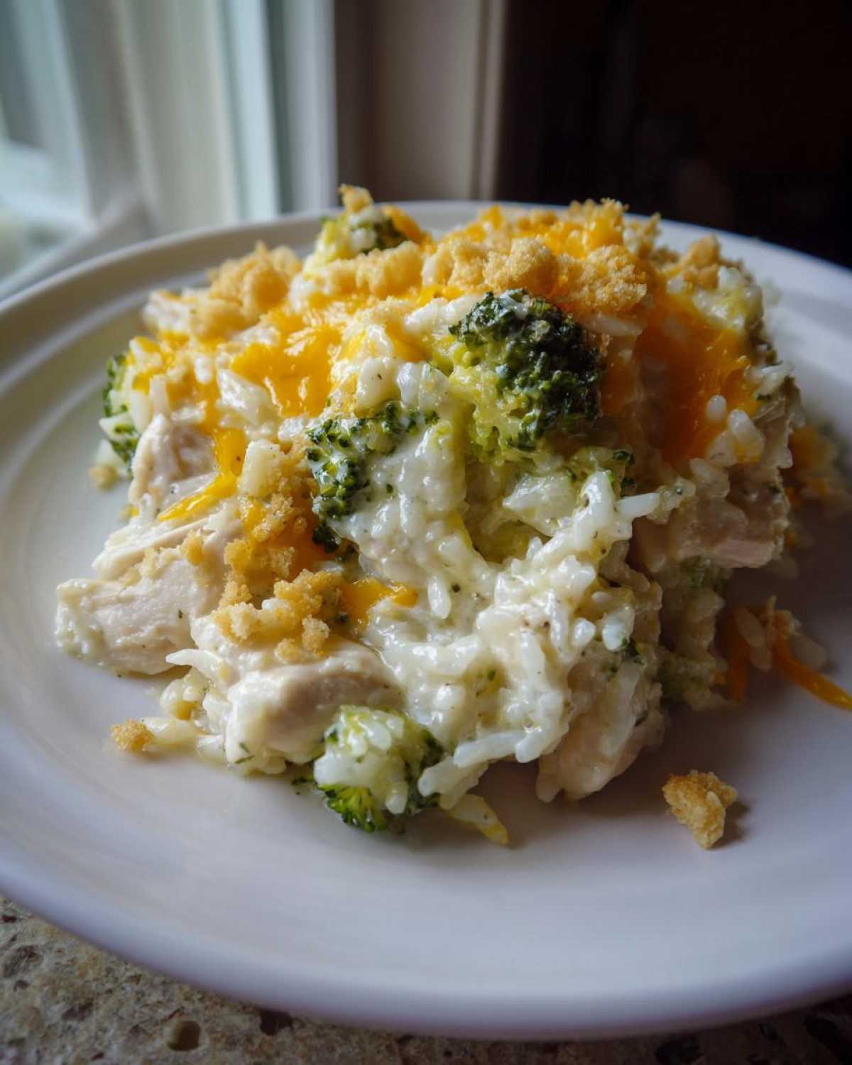 A close-up serving of creamy chicken broccoli rice casserole topped with melted cheddar cheese and breadcrumbs.