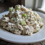 A generous serving of creamy cottage cheese chicken salad mixed with celery and red onion on a white plate.