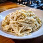 Close-up of fettuccine pasta generously coated in rich homemade alfredo sauce, served on a white plate.
