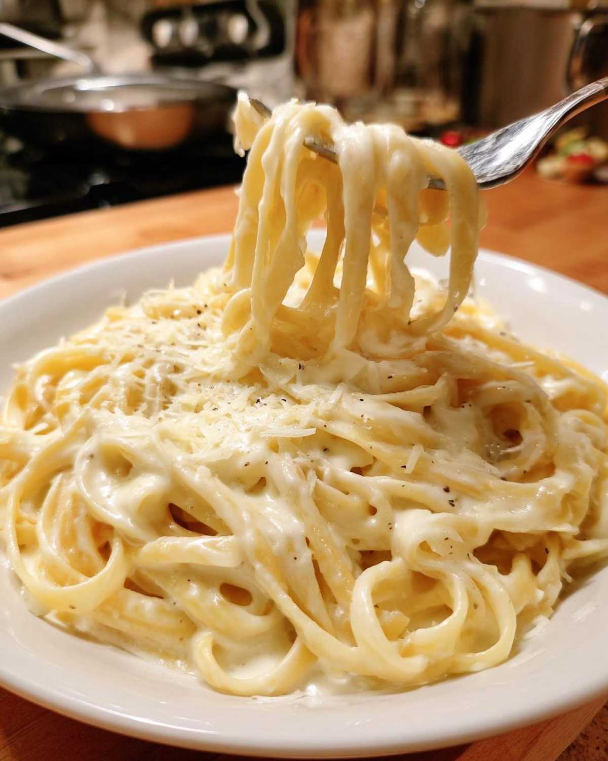A fork lifts creamy fettuccine noodles coated in rich homemade alfredo sauce, topped with grated Parmesan cheese.
