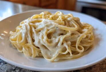 A close-up of fettuccine pasta generously coated in rich, creamy homemade alfredo sauce on a white plate.