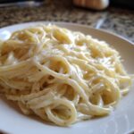 Close-up of fettuccine pasta coated in rich, creamy olive garden alfredo sauce on a white plate.