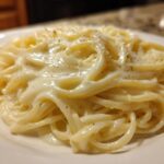 Close-up of fettuccine noodles generously coated in rich, creamy olive garden alfredo sauce and sprinkled with black pepper.