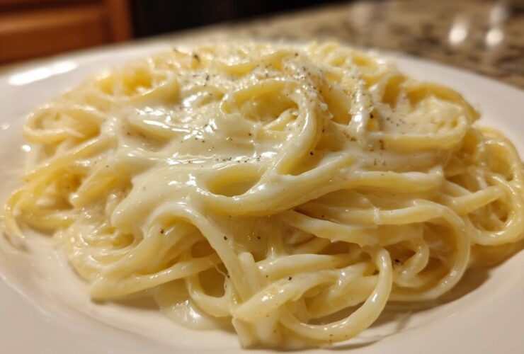 Close-up of fettuccine noodles generously coated in rich, creamy olive garden alfredo sauce and sprinkled with black pepper.