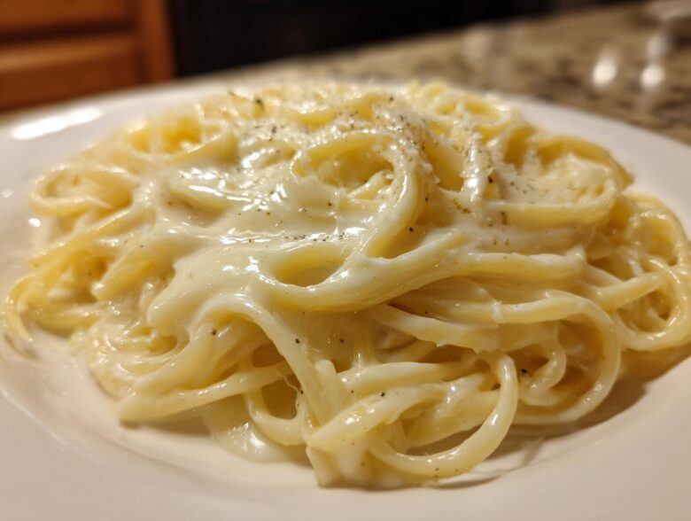 Close-up of fettuccine noodles generously coated in rich, creamy olive garden alfredo sauce and sprinkled with black pepper.