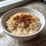 Close-up of a white bowl filled with creamy rice pudding generously dusted with ground cinnamon.