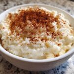 Close-up of a white bowl filled with creamy rice pudding topped generously with ground cinnamon.