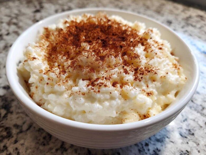 Close-up of a white bowl filled with creamy rice pudding topped generously with ground cinnamon.