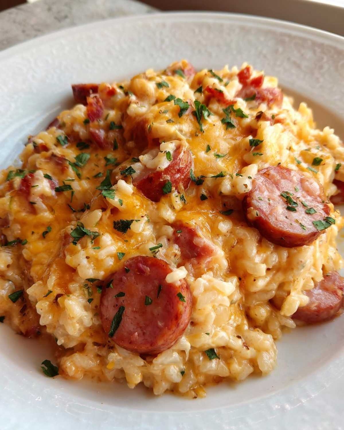 Close-up of creamy sausage and rice mixed with melted cheddar cheese and topped with parsley.