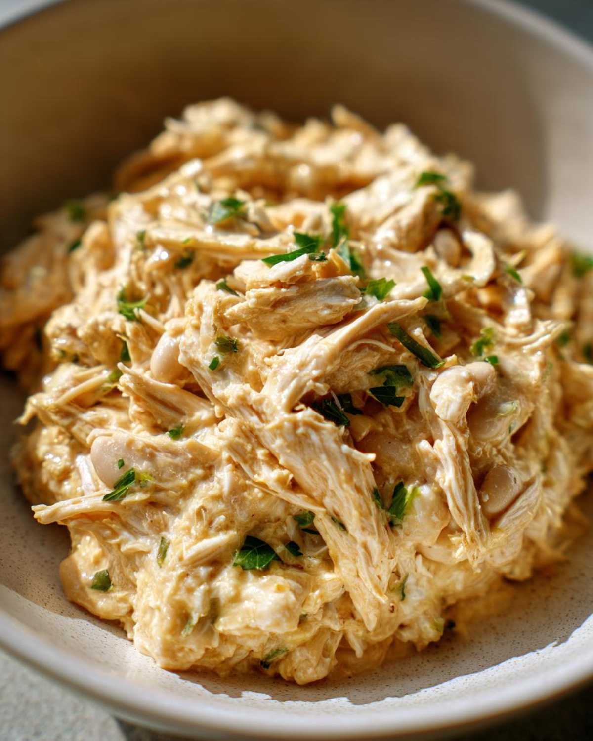 Close-up of creamy, shredded chicken and white beans, garnished with parsley, from crockpot white chicken chili.